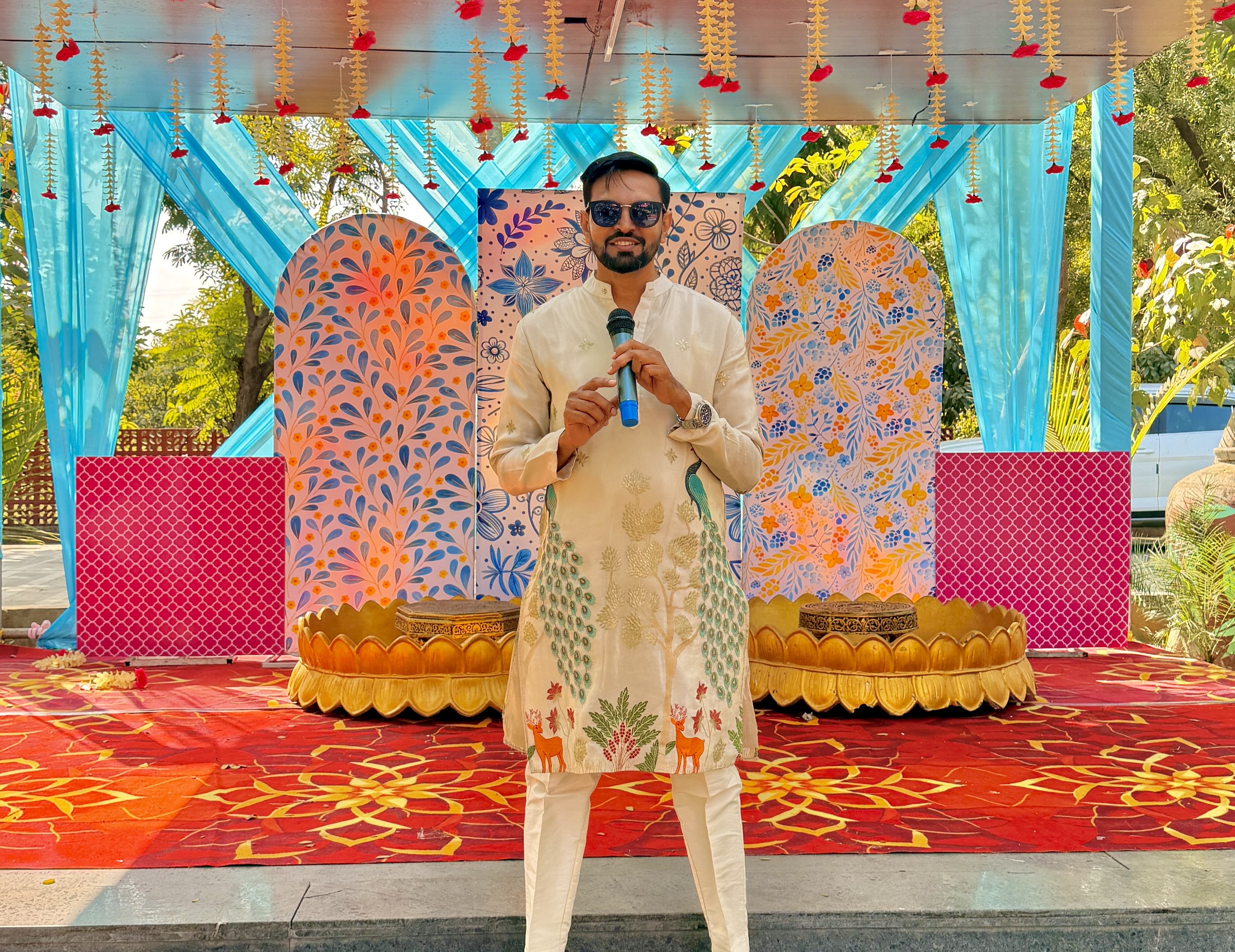 Anchor Nikunj hosting a grand Indian wedding event on stage with a microphone